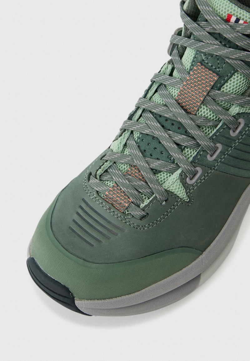 Grüner Wanderschuh mit strukturiertem Design, Mesh-Einsätzen, grauen Schnürsenkeln, strukturierten Akzenten, Gummisohle und Belüftungsöffnungen.