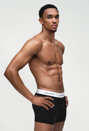 Černé boxerky s geometrickým vzorem a bílým pasem značky Calvin Klein. Látka působí hladce a elasticky.