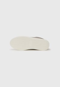 Sneaker sole with a textured white rubber bottom and a smooth beige upper. Features a logo box in the center, with herringbone tread pattern.