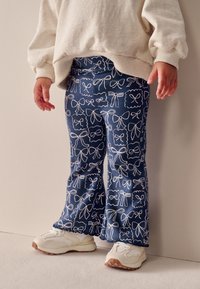 Pantaloni svasati in velluto a coste blu con fiocco bianco e motivi a cornice. Indossati con sneakers bianche, caratterizzate da una tomaia texturizzata e suola in gomma.