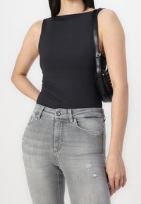 Mujer con top sin mangas negro y jeans grises desgastados con pequeños desgarros, llevando un bolso negro de hombro en su hombro derecho.