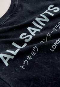 Musta kangas, jossa iso valkoinen teksti "ALLSAINTS" ja pienemmät japanilaiset merkit sekä alhaalla sana "LONDON".