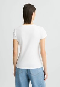T-shirt en coton blanc à manches courtes, avec un col rond et une coupe ajustée, associé à un jean large bleu clair.