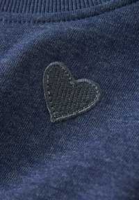 Tessuto a maglia blu scuro con una piccola toppa a forma di cuore ricamata nera vicino al bordo del colletto.