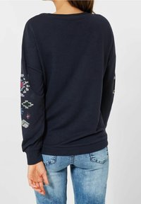 Felpa blu navy con maniche lunghe, orlo a costine e motivo decorativo sulle maniche con paillettes colorate. Vestibilità casual.