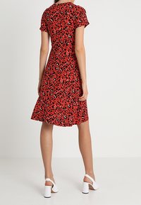 Czerwona sukienka w wzór panterki z krótkimi rękawami, rozkloszowanym dołem i gładką fakturą. Połączona z białymi sandałami na słupku.