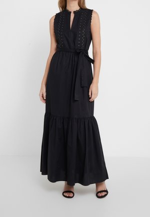 Robe maxi noire sans manches avec panneaux en dentelle ajourée, encolure festonnée, ceinture nouée à la taille et ourlet volanté, portée avec des talons noirs ouverts à l'avant.