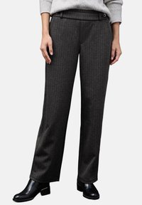 Pantalones grises de rayas con un corte ajustado, hechos de una tela texturizada. Cuentan con un frente plano, pasadores para cinturón y bolsillos laterales. Llevados con botas negras de tobillo.