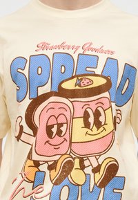 Χαμογελαστή καρτούν φέτα ψωμί και βαζάκι με μαρμελάδα φράουλα κρατιούνται χέρι-χέρι και περπατούν, με το κείμενο «Strawberry Goodness ΔΙΑΔΩΣΕ ΤΗΝ ΑΓΑΠΗ» σε κρεμ πουκάμισο.