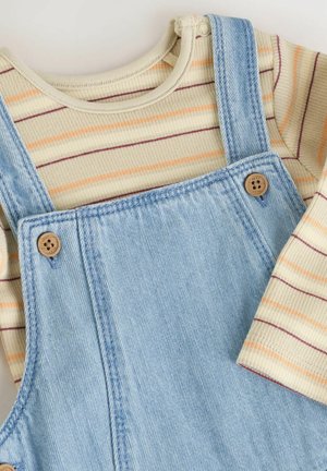 Beige gestreiftes Langarmhemd, in hellblaue Jeansoverall mit Holzknöpfen gesteckt, vor einem neutralen Hintergrund präsentiert.