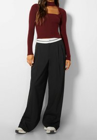 Top de manga larga acanalado burdeos con escote cuadrado, combinado con pantalones de pierna ancha negros de talle alto que presentan una cinturilla con acentos blancos.