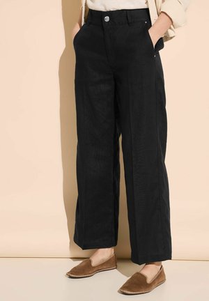 Pantaloni neri a gamba larga realizzati in lino con una finitura testurizzata, dotati di tasche frontali e chiusura con bottone argentato. Scarpe marroni slip-on completano il look.