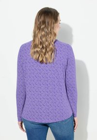 Fioletowa koszula z długim rękawem w powtarzający się wzór róż; miękka tekstura i luźny krój, zestawiona z jasnoniebieskimi dżinsami.