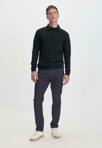 Donkergrijze pullovertrui met een kraag, gedragen over blauwe jeans en witte sneakers. Eenvoudig ontwerp met geribbelde manchetten en zoom.