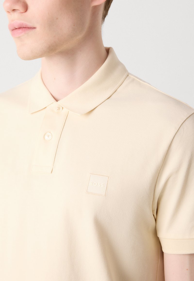 Polohemd in zartbeige, aus strukturiertem Stoff. Verfügt über einen klassischen Kragen, zwei Knöpfe und ein kleines quadratisches Logo in einer tonalen Farbe.