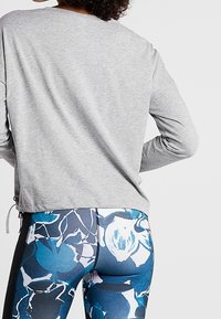 Grå långärmad topp med rund halsringning och dragsko-detalj. Leggings med blommönster i blått, svart och vitt med en slimmad design.