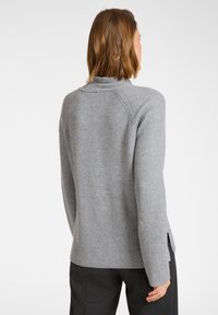 Szary prążkowany sweter z długimi rękawami, posiadający wysoki dekolt i boczne rozcięcia u dołu. Miękka dziana struktura i dopasowany krój.