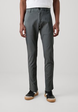 Gray cotton blend trousers with a slim fit, flat front, and button closure. Worn with black sneakers featuring white accents.