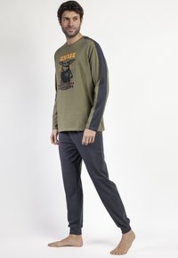 Camiseta de manga larga color verde oliva con diseño gráfico y mangas azul oscuro, combinada con pantalones jogger gris oscuro con dobladillos ajustados.