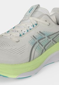 Λευκό αθλητικό παπούτσι Asics με ανοιχτό πράσινο σόλα, πάνω μέρος από δίχτυ, τιρκουάζ λεπτομέρειες και λευκά κορδόνια, που παρουσιάζει λεπτομέρειες από πλάγια και μπροστά.