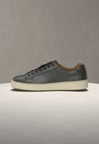 Μαύρο δερμάτινο sneaker με χαμηλό πάνω μέρος, μαύρα κορδόνια και παχύ λευκό καουτσούκ πάτο σε ουδέτερο φόντο.