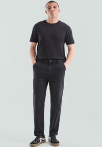 Czarna koszulka, luźny krój, materiał bawełniany; czarne spodnie, tapered design, subtelna tekstura; czarne sneakersy z białymi akcentami, płaska podeszwa.