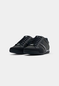 Black athletic shoes with a combination of smooth synthetic upper and suede accents. Features flat laces, rubber sole, and side logo detail.