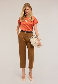 Top di raso arancione, pantaloni marroni a vita alta, borsa beige e sandali con tacco color nude. Include una collana e orecchini come accessori.