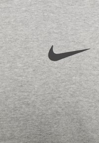 Logo Swoosh nero di Nike su uno sfondo in tessuto lavorato a maglia grigio chiaro, probabilmente un capo di abbigliamento.