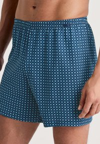 Marineblauwe boxershorts met een geometrisch patroon van lichtblauwe vierkanten. Gemaakt van zachte stof en voorzien van een elastische tailleband voor comfort.