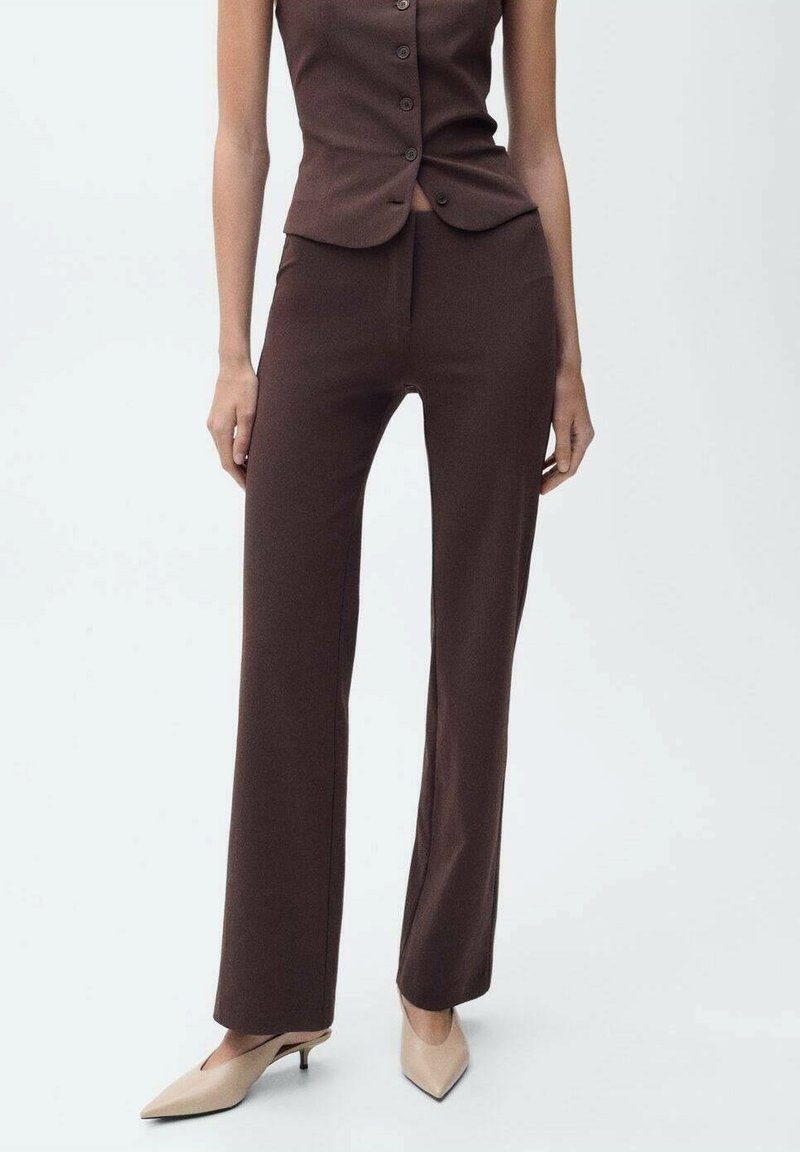 Pantalon marron ajusté en tissu texturé, avec une coupe droite et une taille haute, associé à des escarpins beiges à bout pointu.