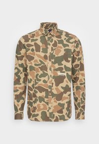 Camicia con motivo camouflage in beige, verde e marrone. Presenta un design con bottoni, colletto e taschino sul petto sinistro. "ORIGINALS" è stampato sul davanti.