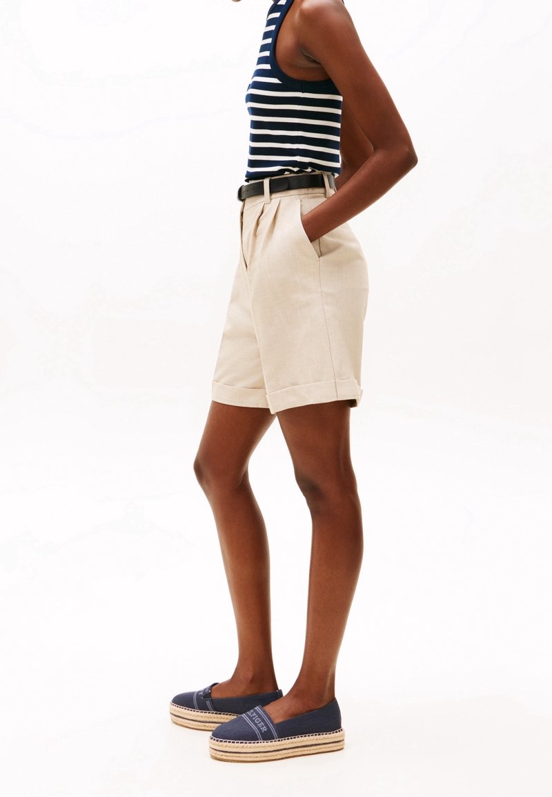 Femme portant un short plissé beige, une ceinture noire, un débardeur rayé bleu marine et des espadrilles bleu marine à semelles compensées.