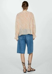 Blouse légère à manches longues avec un motif floral pastel, associée à un short en denim. Les sandales présentent des brides croisées au niveau des chevilles.