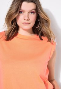 Oranje oversized mouwloze top met een ronde halslijn. Glad materiaal, zachte textuur en subtiele stikdetails.