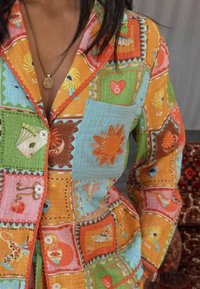 Patchwork kleding met levendige kleuren zoals oranje, blauw en groen, verfraaid met geborduurde accenten zoals bloemen en harten, gemaakt van zachte stof.