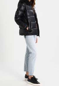 Svart vadderad jacka med huva och quiltade sektioner. Kombinerad med ljusblå jeans med raka ben och svarta sneakers.