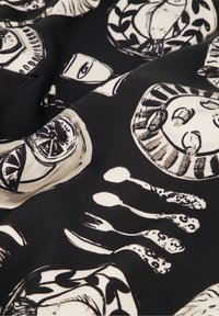 Zwarte stof met een herhalend wit patroon dat gezichten, gebruiksvoorwerpen en decoratieve elementen toont. Soepele textuur met grafische illustraties.