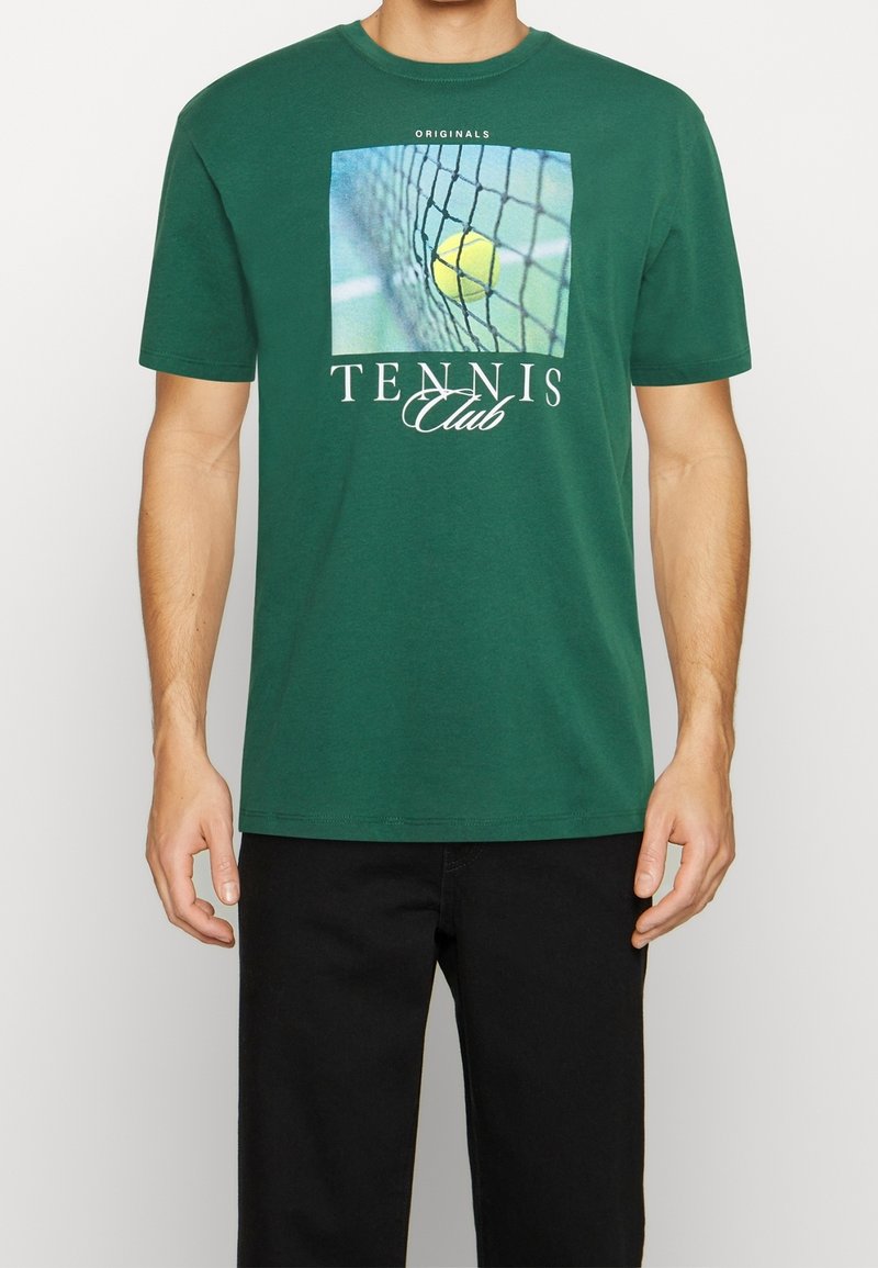 Grön bomullströja med en tennisgrafik som visar en boll och nät, samt texten "Tennis Club" i vitt. Korta ärmar och rundad halsringning.