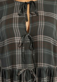 Blusa a cuadros en verde oscuro y gris, con un escote atado y un fondo acampanado y fruncido. Tejido ligero con una textura suave.