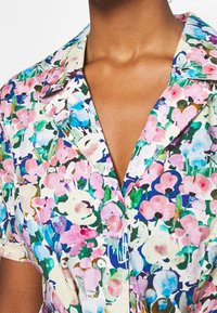 Wielokolorowa sukienka koszulowa w lekkim materiale, z kołnierzykiem, krótkimi rękawami i różowymi guzikami, ozdobiona żywym wzorem kwiatów.