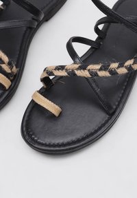 Sandalias de cuero negro con acentos de mimbre trenzado y correas entrecruzadas. Suelas planas con un acabado suave y un diseño minimalista.