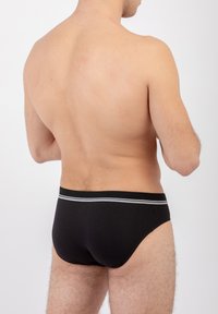 Slip black in cotone con una vestibilità aderente, caratterizzato da un design semplice e una vita elastica grigia a contrasto. Texture liscia senza motivi visibili.