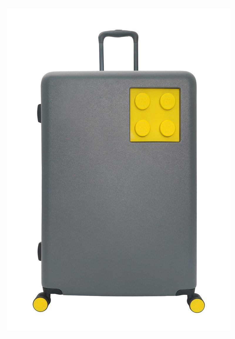 Gray hard-shell suitcase with a yellow LEGO-style accent featuring four circular bumps. Retractable handle and yellow wheels for mobility.