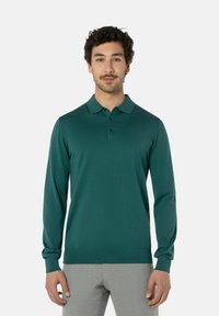 Tropfblaues Langarm-Polohemd mit Kragen, dreiknöpfiger Placket und gerippten Bündchen. Glatte Textur, taillierte Passform, kombiniert mit hellgrauen Hosen.