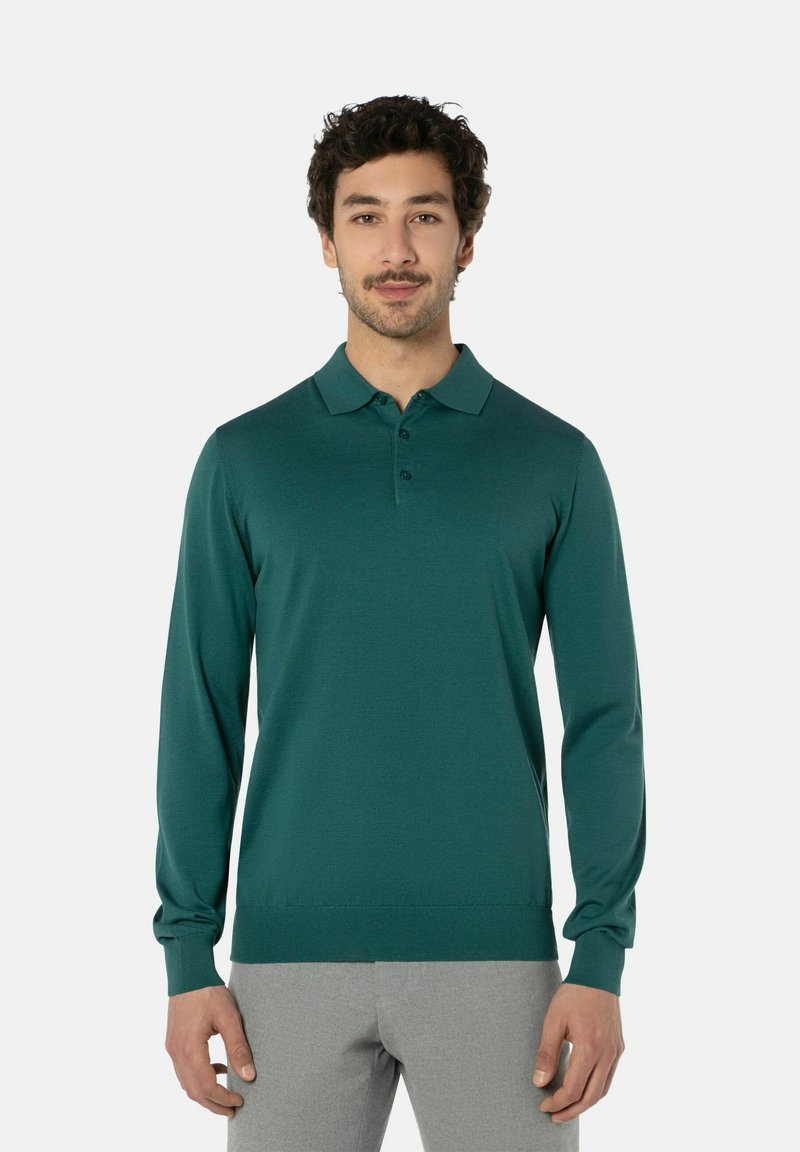 Tropfblaues Langarm-Polohemd mit Kragen, dreiknöpfiger Placket und gerippten Bündchen. Glatte Textur, taillierte Passform, kombiniert mit hellgrauen Hosen.