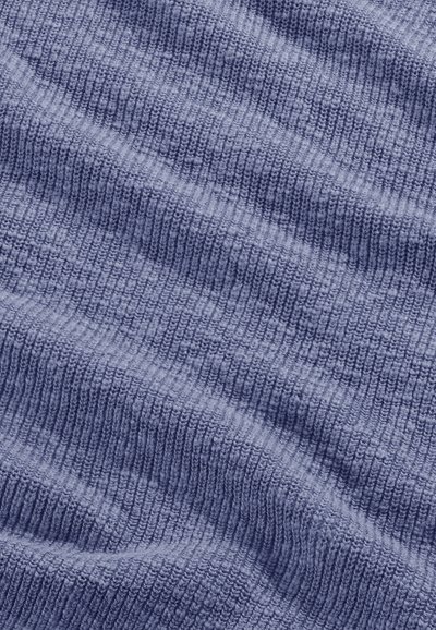 Gros plan sur un tissu bleu côtelé doux avec un motif tricoté texturé visible et de légers plis créant des zones ombragées.