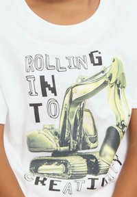 Weißes Baumwoll-T-Shirt mit einem Grafikdruck eines gelben Baggers und dem Text "ROLLING INTO CREATIVITY" in schwarzer, abgenutzter Schrift.