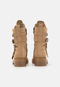 Botas de tornozelo em suede bege com biqueira arredondada, apresentando dois detalhes de tiras ajustáveis e um zip lateral, assentes num salto bloco texturizado.