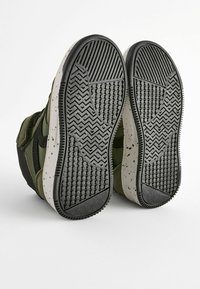 Groene en zwarte hoge sneakers met gestructureerde rubberen zolen, voorzien van een gespikkelde witte tussenzool en een patroonontwerp in de loop.